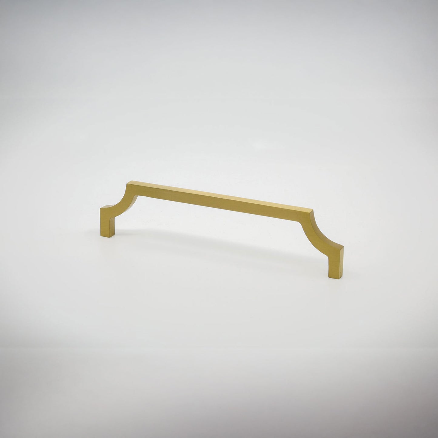 A single satin brass cabinet pull handle with curved edges against a seamless light gray studio background.