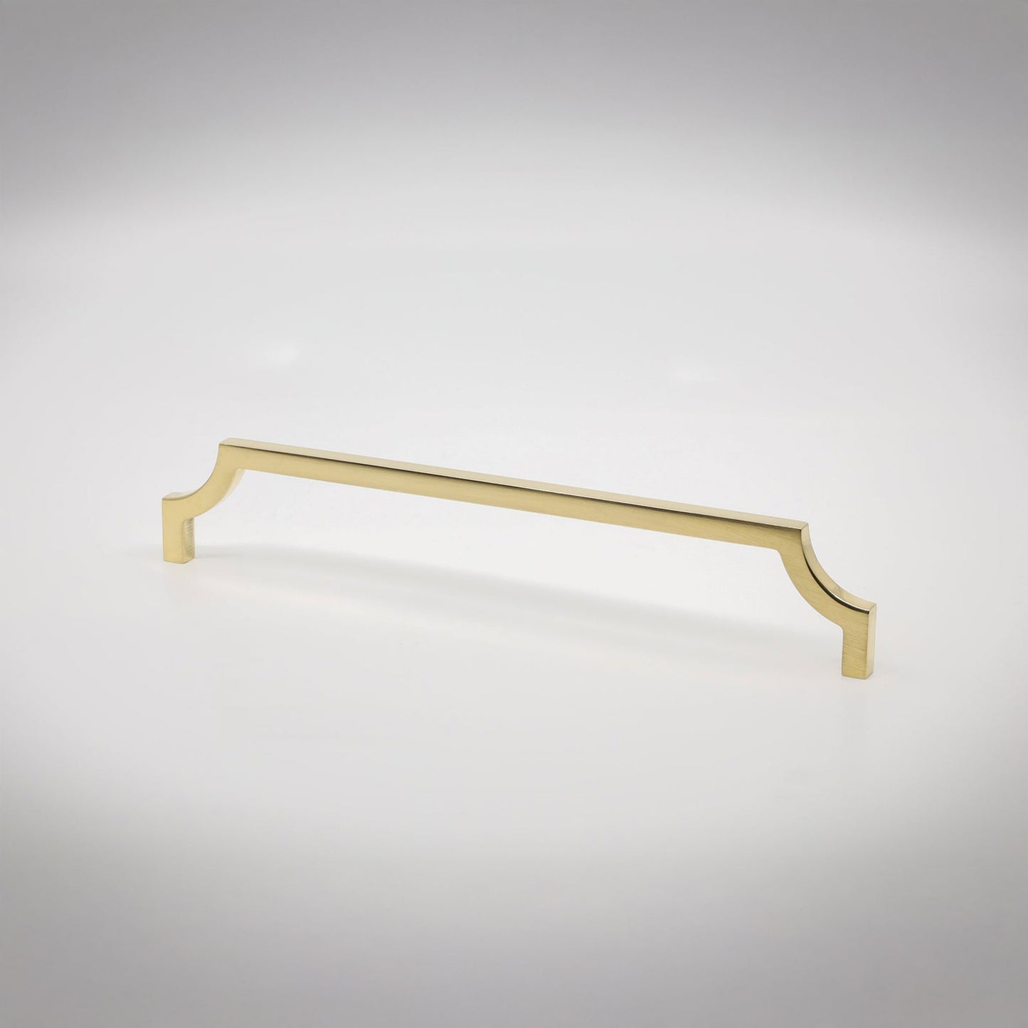 A single long cabinet pull handle with a polished unlaquered brass finish, featuring decorative scrolled ends, shown on a light gray gradient background.