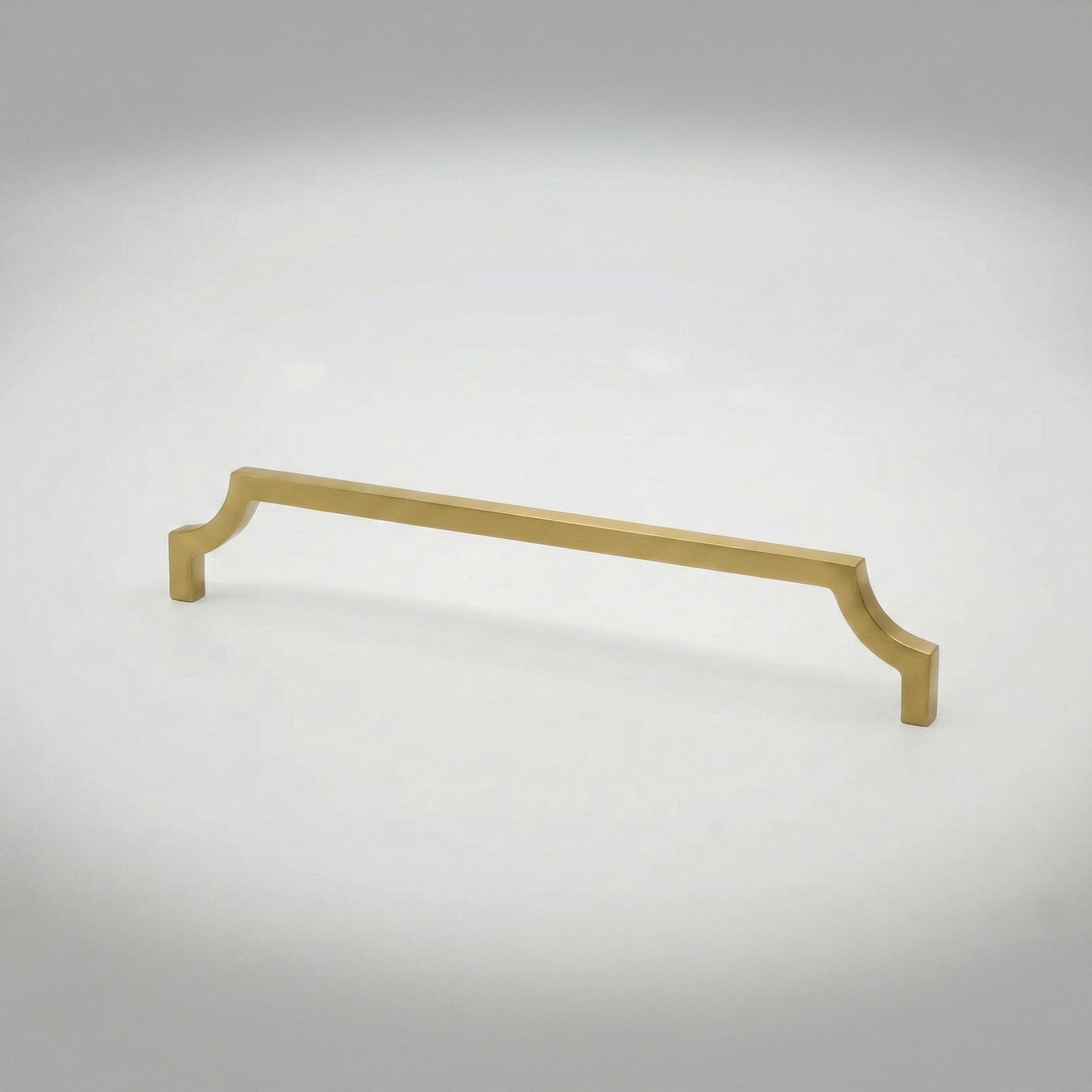 A satin brass cabinet pull handle with curved edges against a light gray studio background.