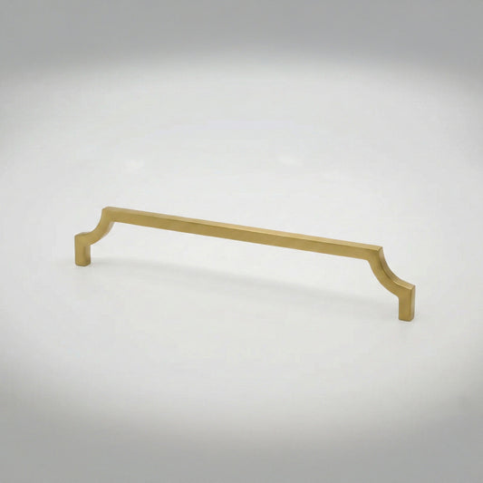 A satin brass cabinet pull handle with curved edges against a light gray studio background.
