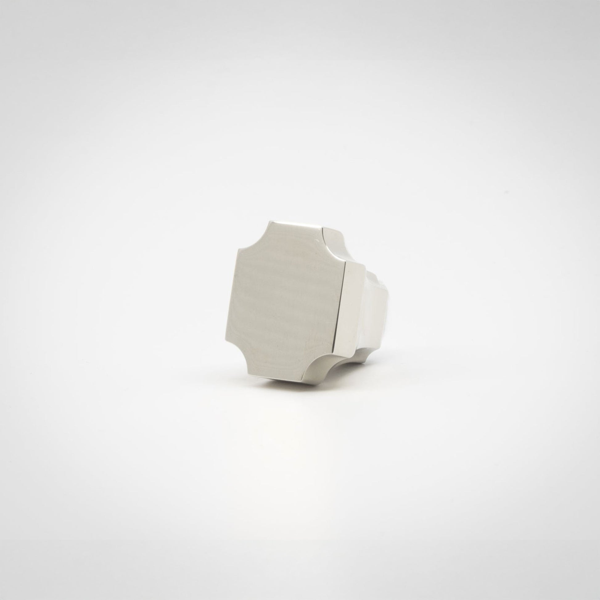 A small polished nickel knob with a geometric, faceted shape, photographed on a seamless white background.
