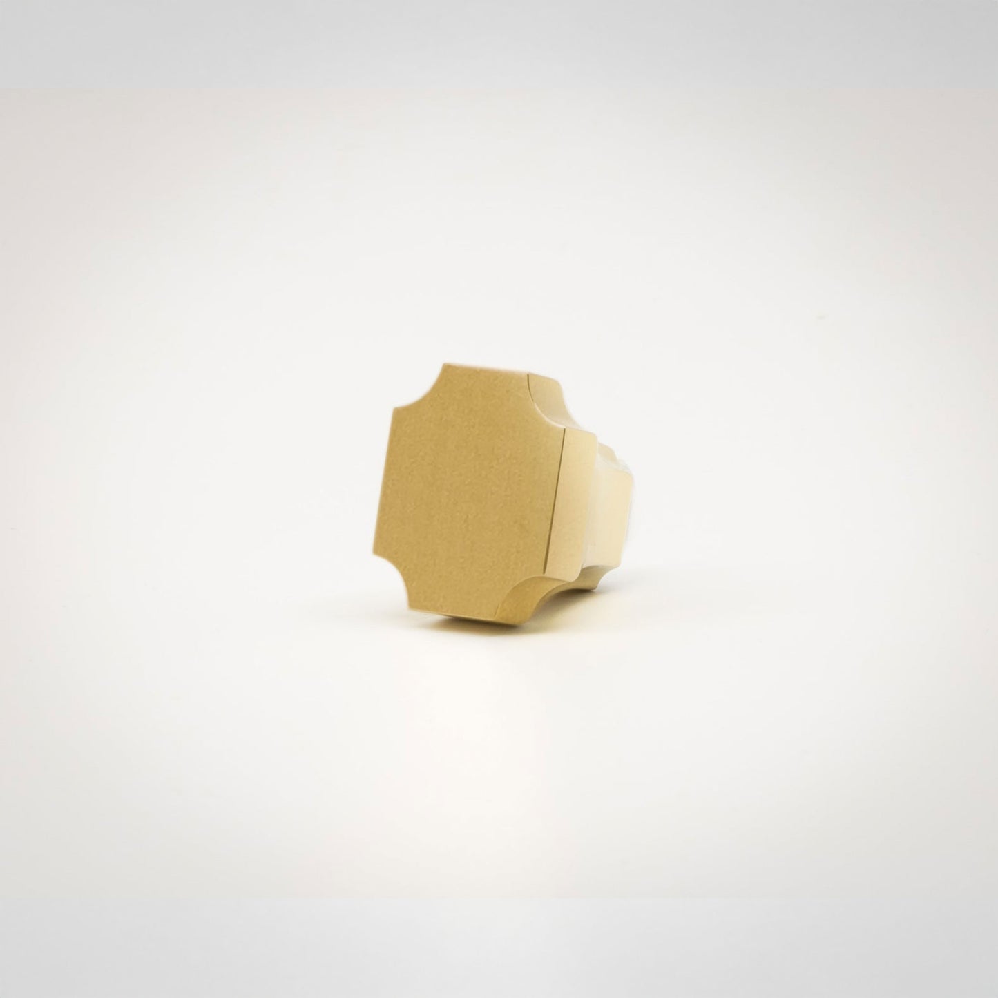 A small brass hardware knob with a geometric, faceted shape, photographed on a seamless white background.