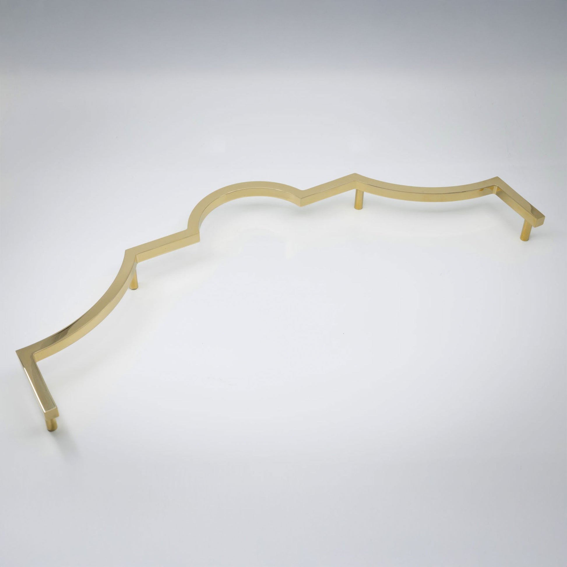 A long decorative cabinet pull handle with a wavy scalloped edge, in a polished unlacquered brass shown on a clean light gray studio background.