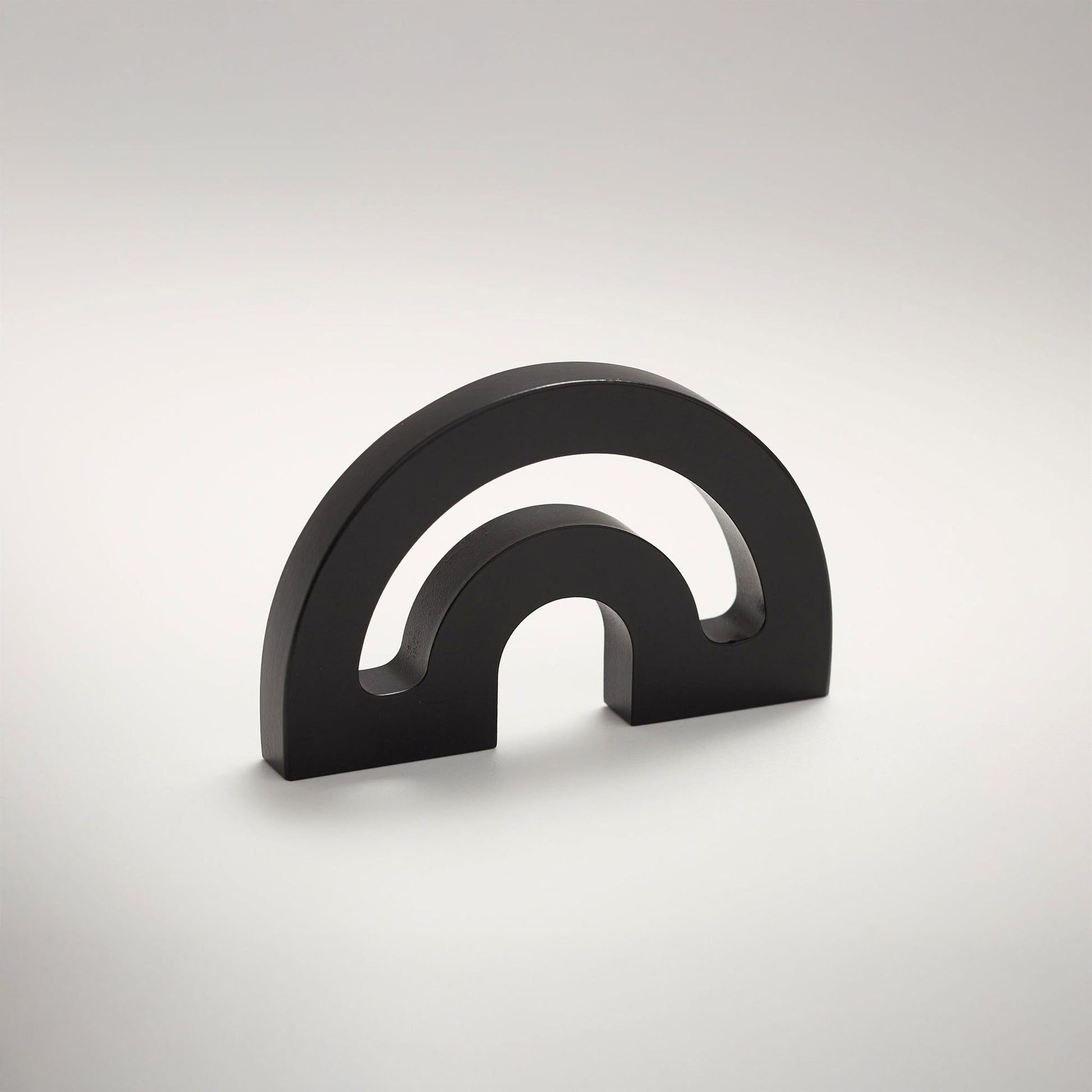 A minimalist metal cabinet knob with a double-arch design, photographed on a clean light gray gradient background.