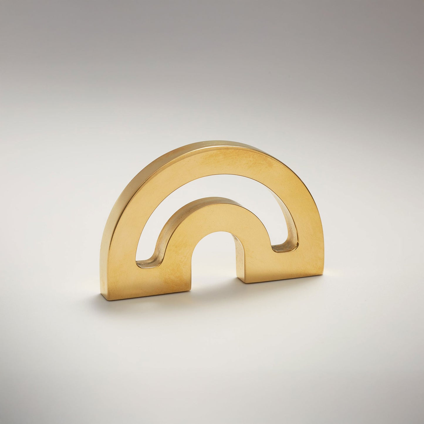 A minimalist metal cabinet knob with a double-arch design, photographed on a clean light gray gradient background.