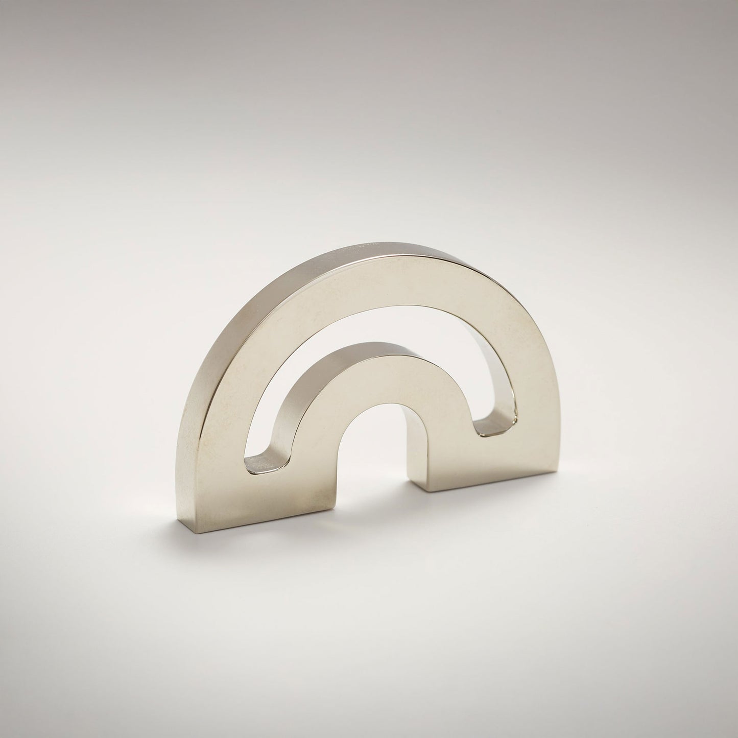 A minimalist metal cabinet knob with a double-arch design, photographed on a clean light gray gradient background.
