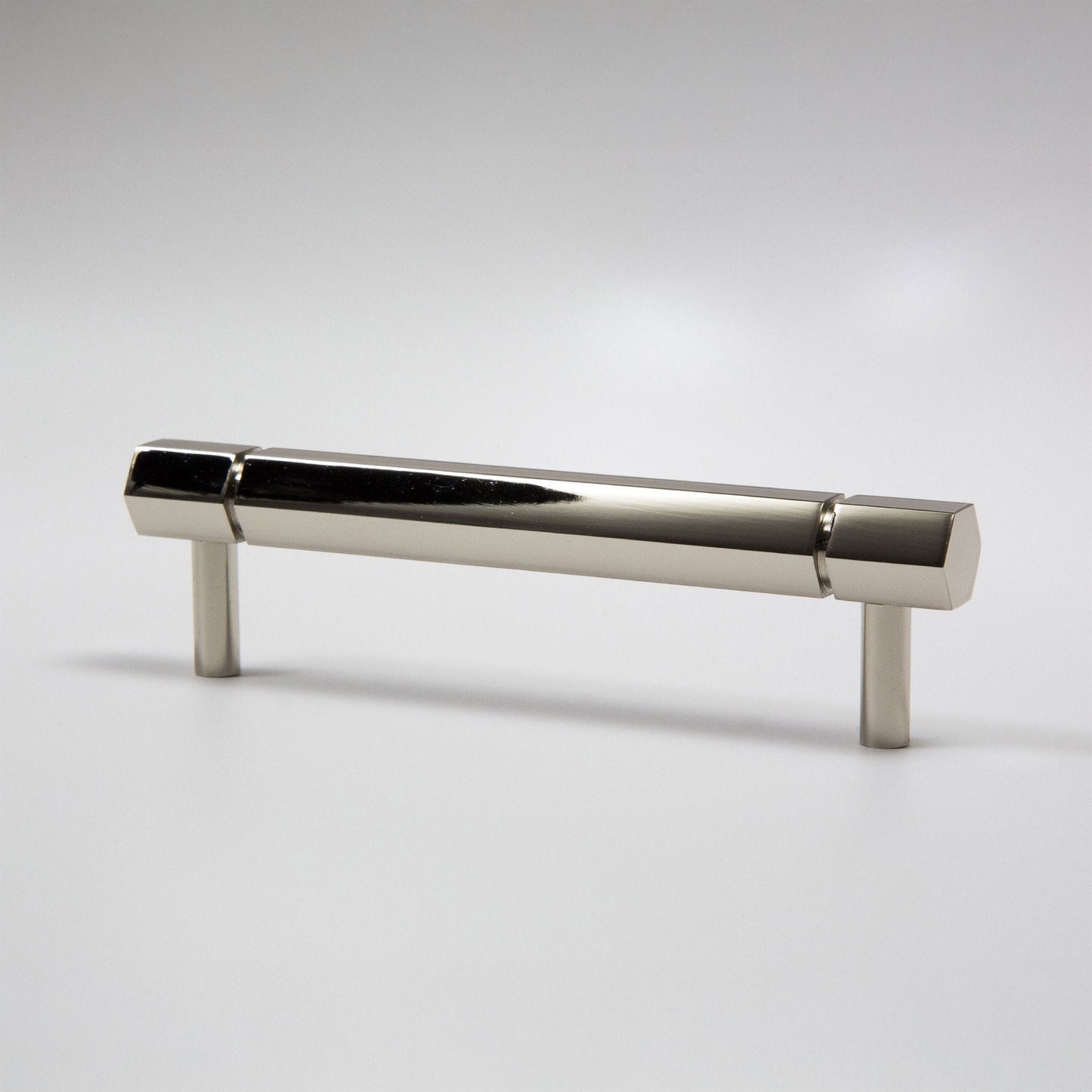 A modern hexagonal cabinet handle in polished nickel, featuring a long horizontal bar supported by two short cylindrical posts, shown on a light gray background.