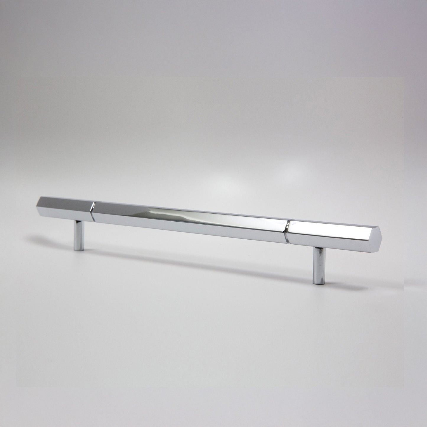 A modern hexagonal cabinet handle in polished chrome featuring a long horizontal bar supported by two short cylindrical posts, shown on a light gray background.