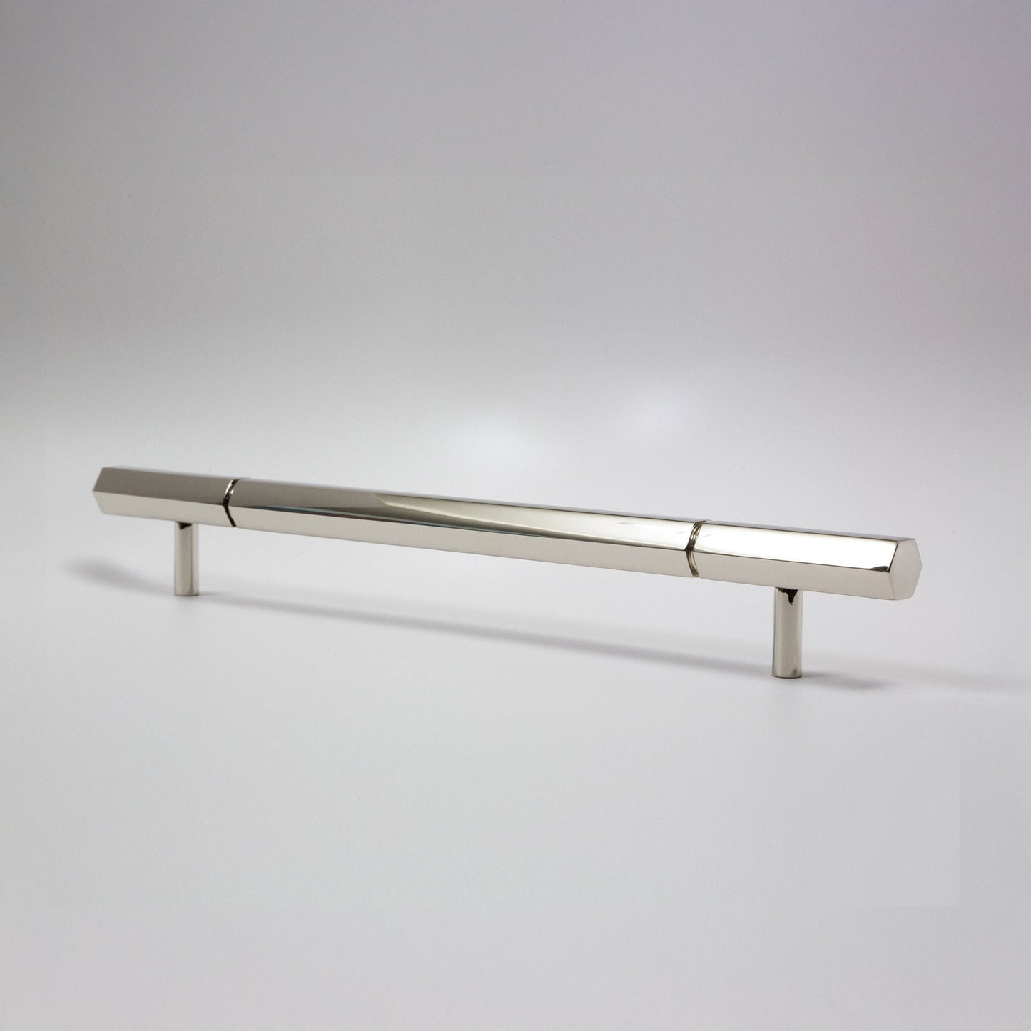 A modern hexagonal cabinet handle in polished nickel, featuring a long horizontal bar supported by two short cylindrical posts, shown on a light gray background.