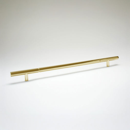 A modern hexagonal cabinet handle in unlaquered brass, featuring an extra long horizontal bar supported by two short cylindrical posts, shown on a light gray background.