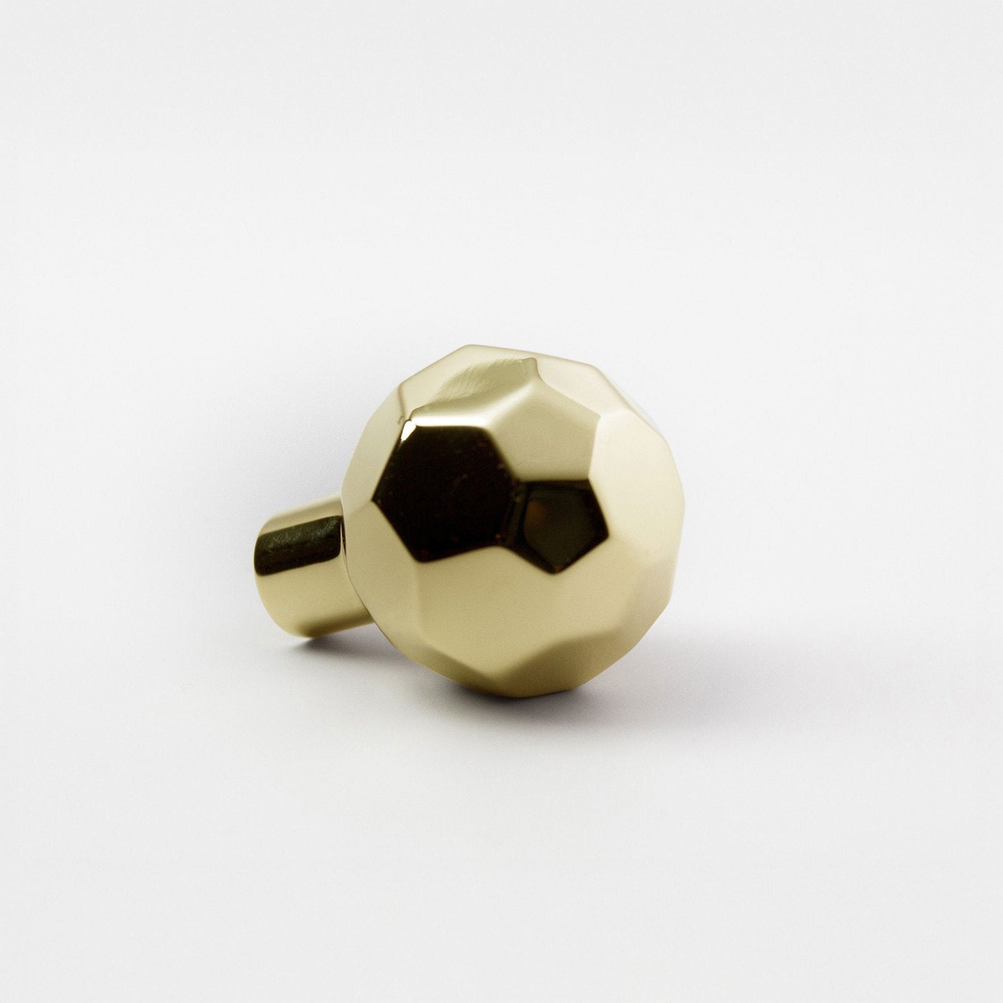 A modern hexagonal cabinet knob in polished brass, with one short cylindrical post, shown on a light gray background.