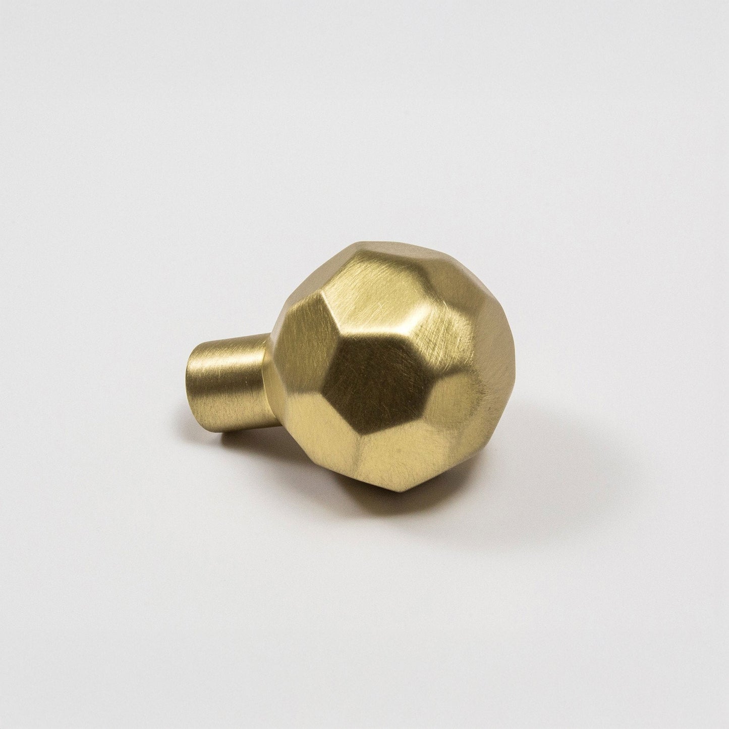 A modern hexagonal cabinet knob in satin brass, with one short cylindrical post, shown on a light gray background.