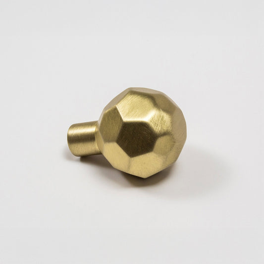 A modern hexagonal cabinet knob in satin brass, with one short cylindrical post, shown on a light gray background.