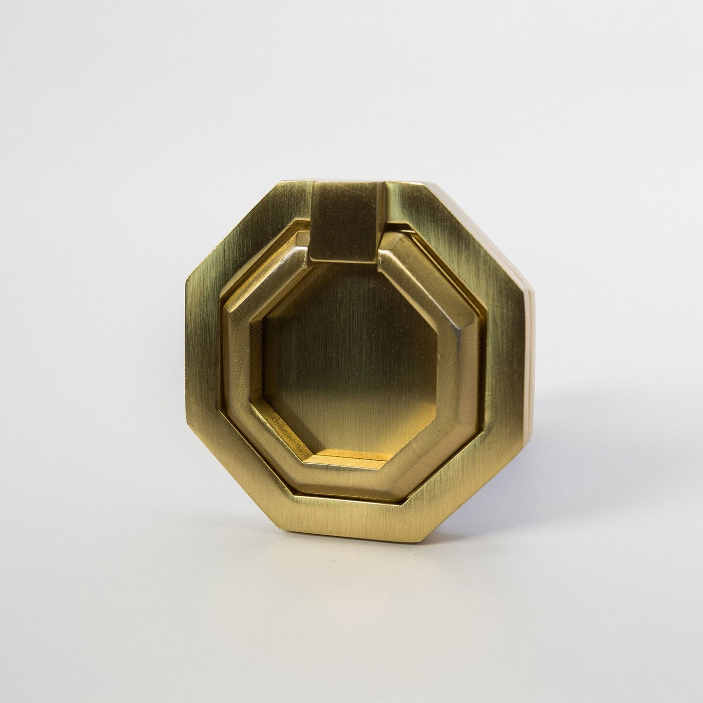 An octagonal metal ring cabinet pull with a satin brass finish, photographed on a clean light gray background.