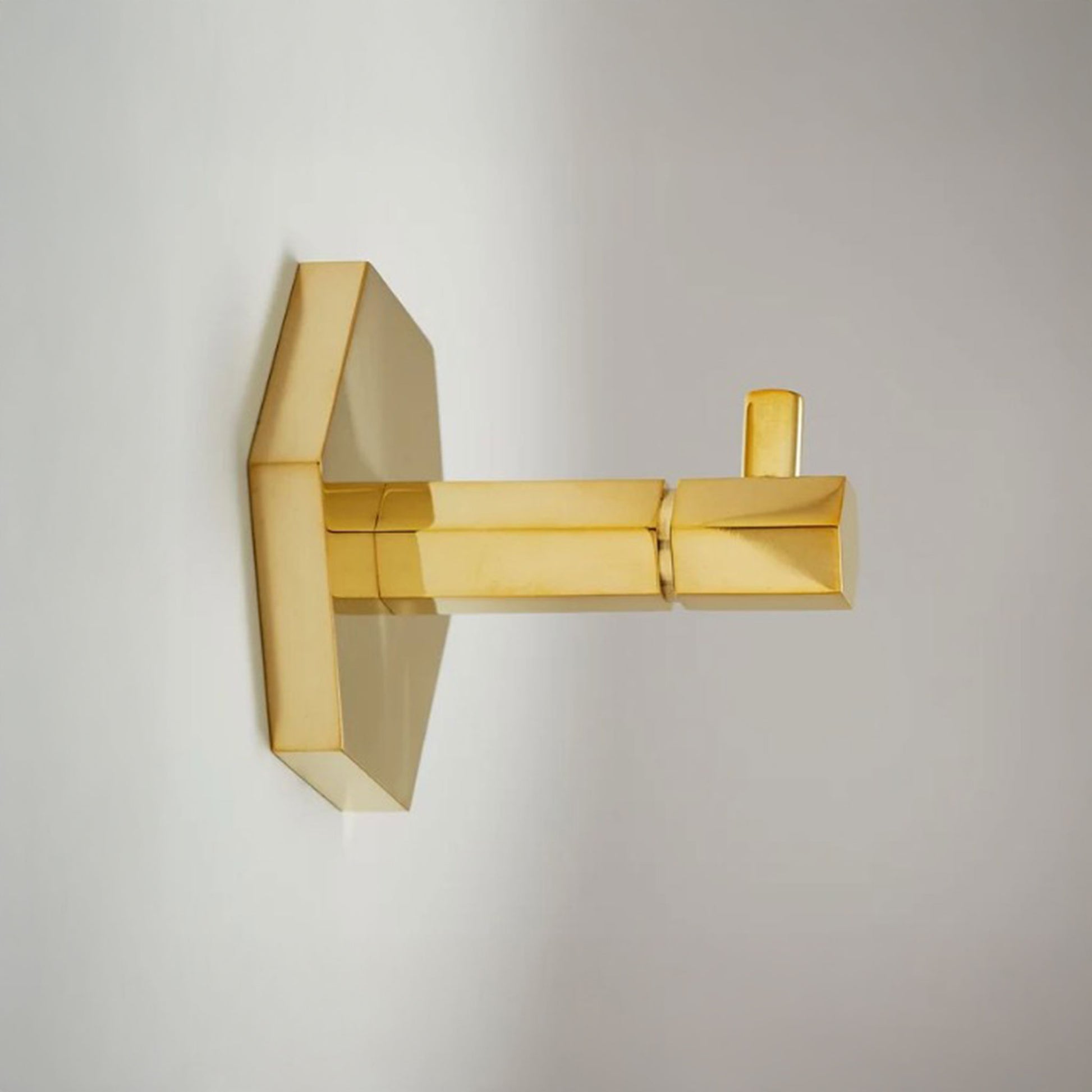 A modern wall-mounted gold towel hook with a geometric, faceted design, shown mounted on a plain light gray wall.