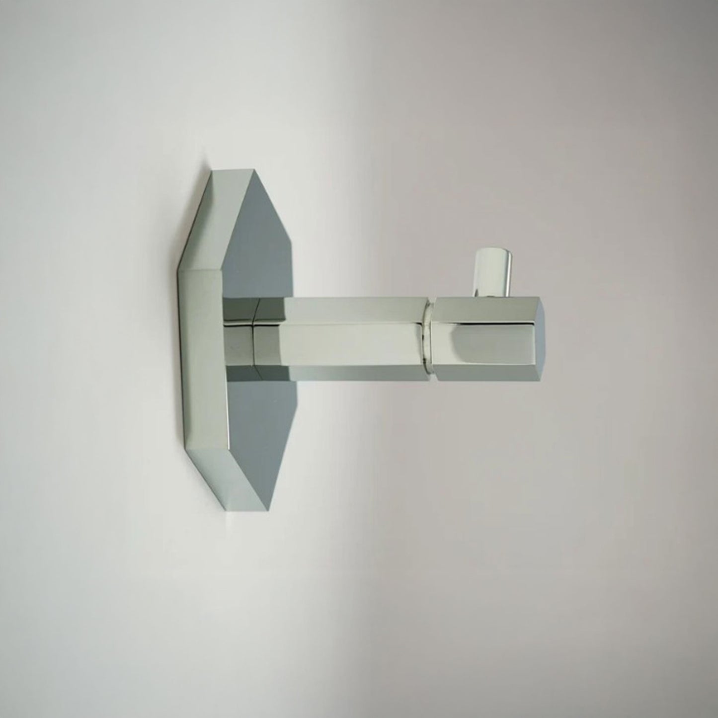 A modern wall-mounted towel hook  with a geometric, angular design in polished chrome, shown against a plain light gray wall.