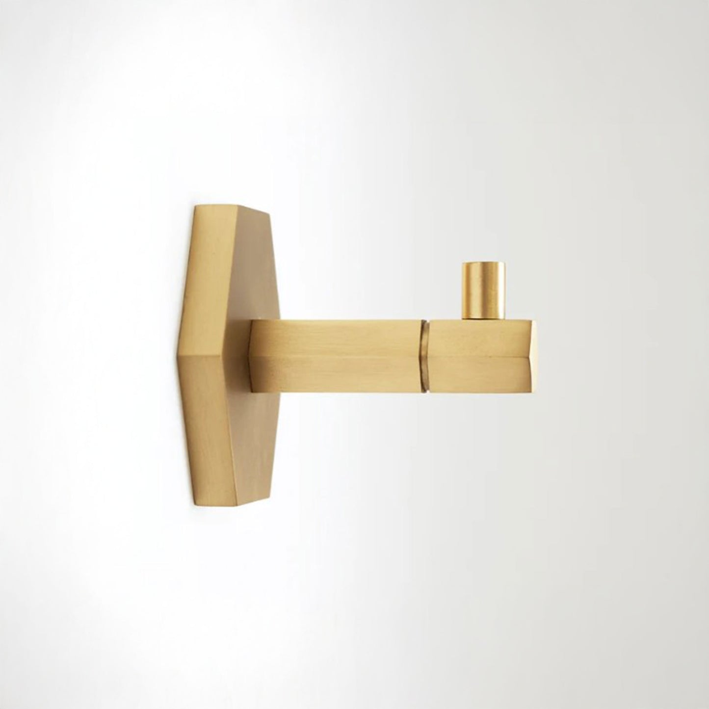 A modern wall-mounted brass fixture with a geometric backplate and a single cylindrical spout, shown against a plain white background.