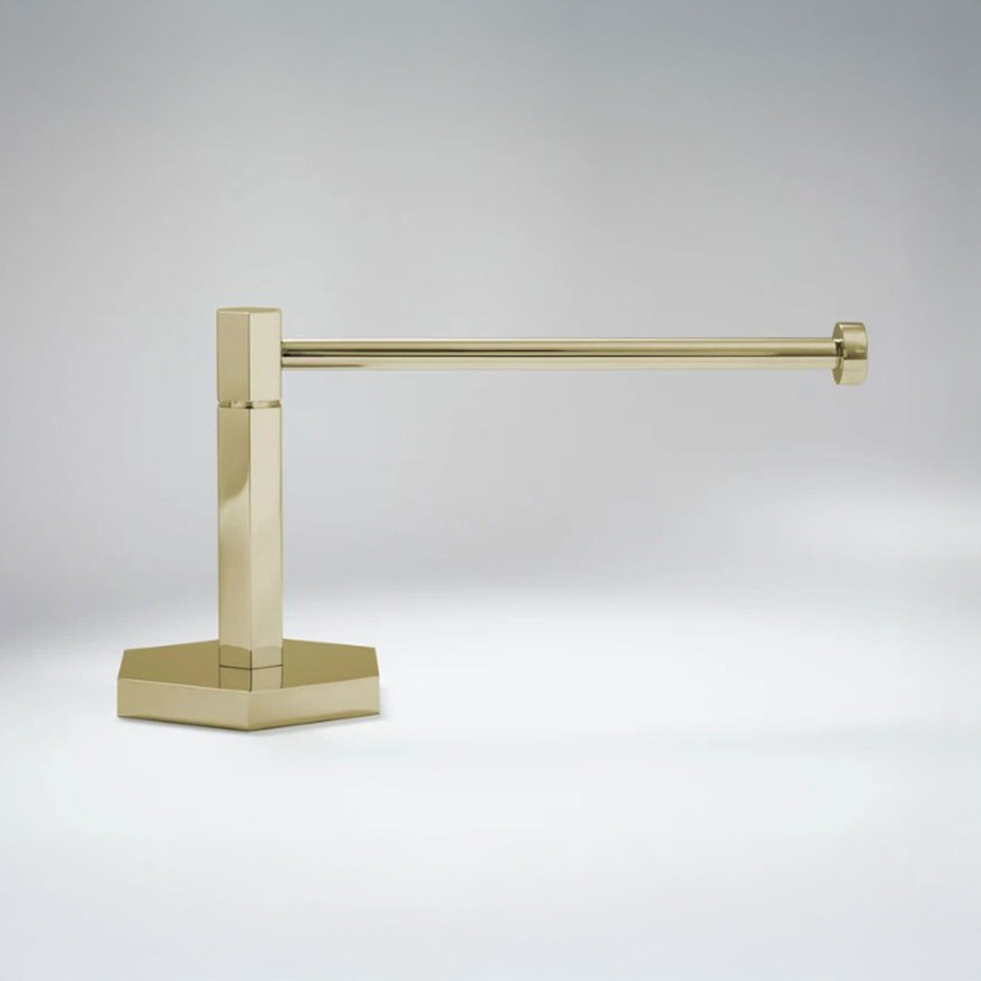 A modern wall-mounted paper holderr with a polished brass finish, featuring a square post and a flat base, shown against a neutral gray background.