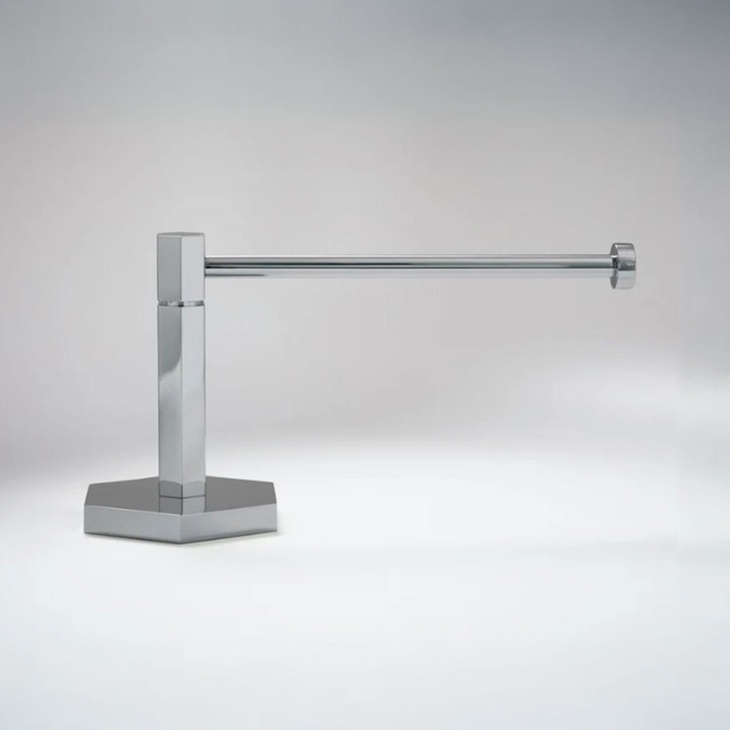 A modern wall-mounted paper holderr with a polished chrome finish, featuring a square post and a flat base, shown against a neutral gray background.