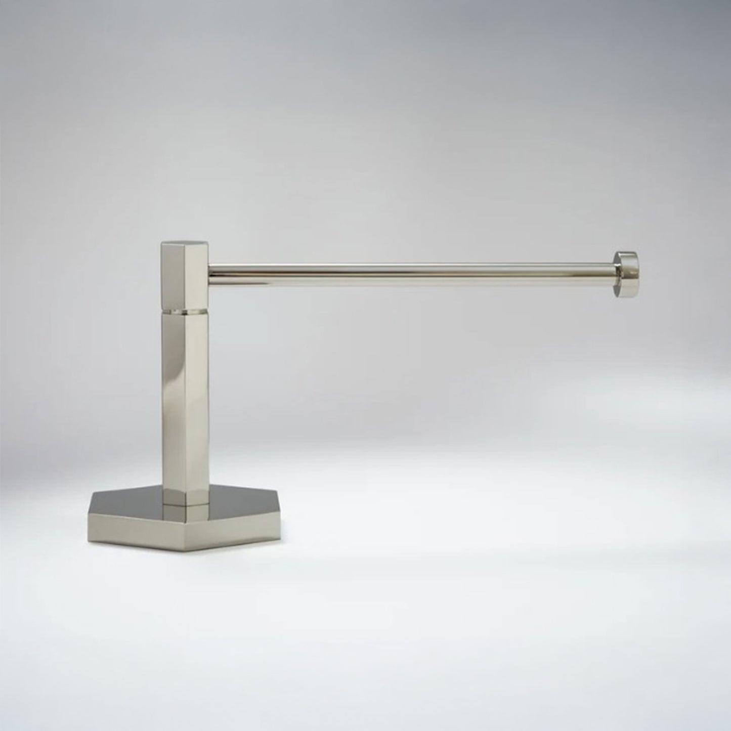 A modern wall-mounted paper holderr with a polished nickel finish, featuring a square post and a flat base, shown against a neutral gray background.