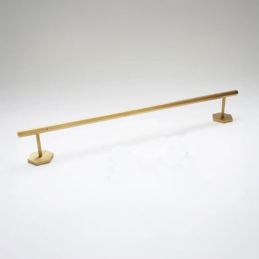 A modern brass towel bar with a sleek, minimalist design, featuring a long horizontal bar supported by two hexagonal bases, shown on a light gray background.