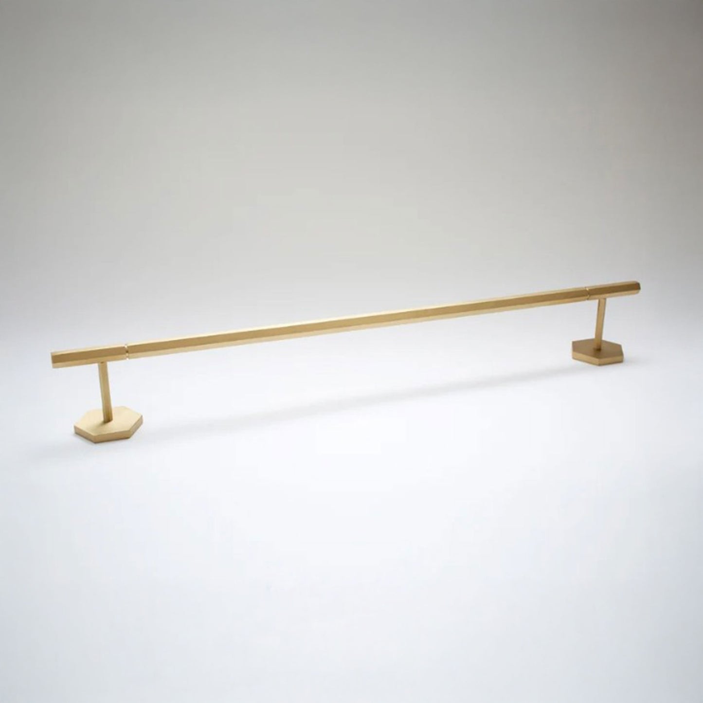 A long, slender gold metal rod with two hexagonal base plates, photographed on a clean light gray studio background.
