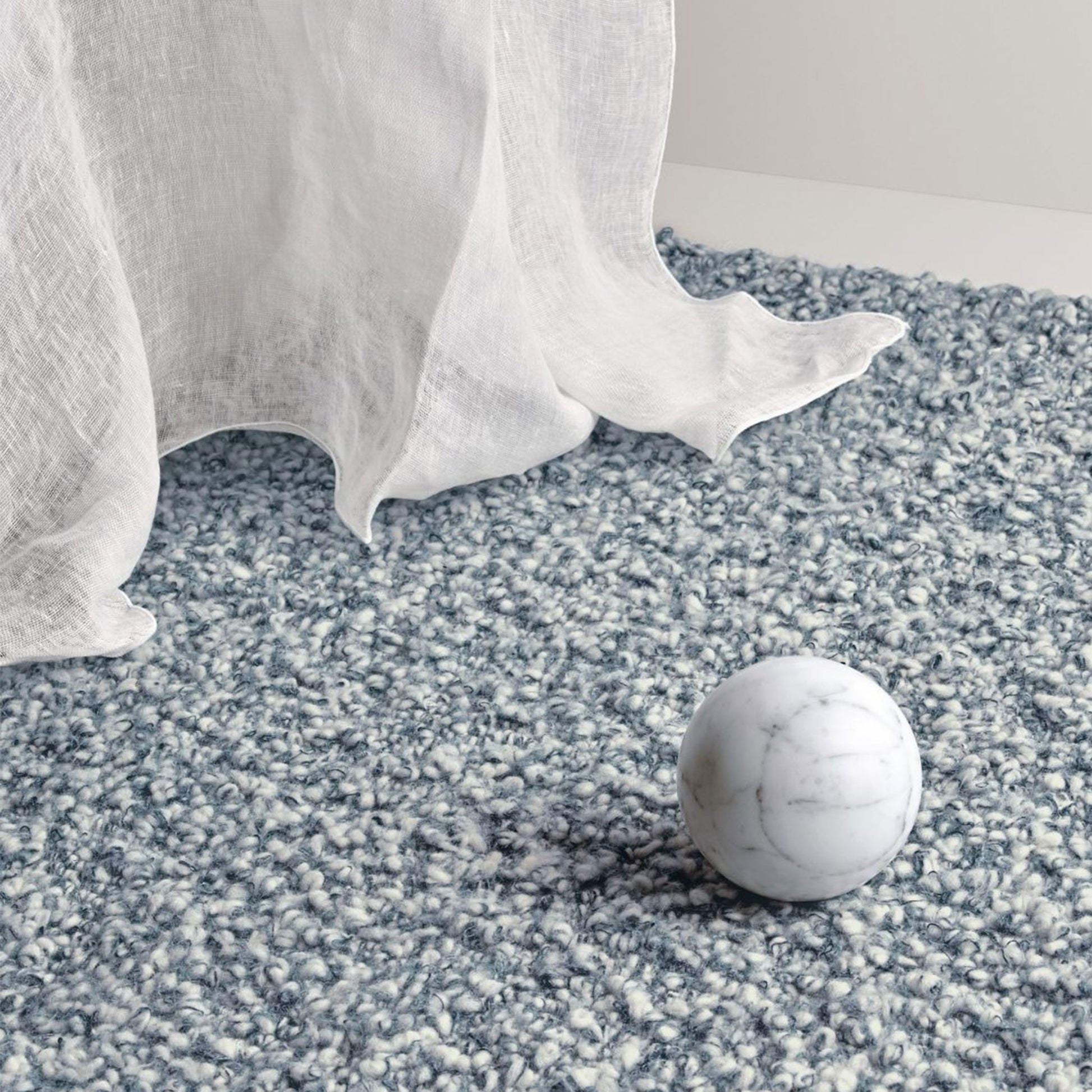 Aria rug style in smoke blue and cream colored twisted textured heavy boucle weave in a room with sheers and a marble ball