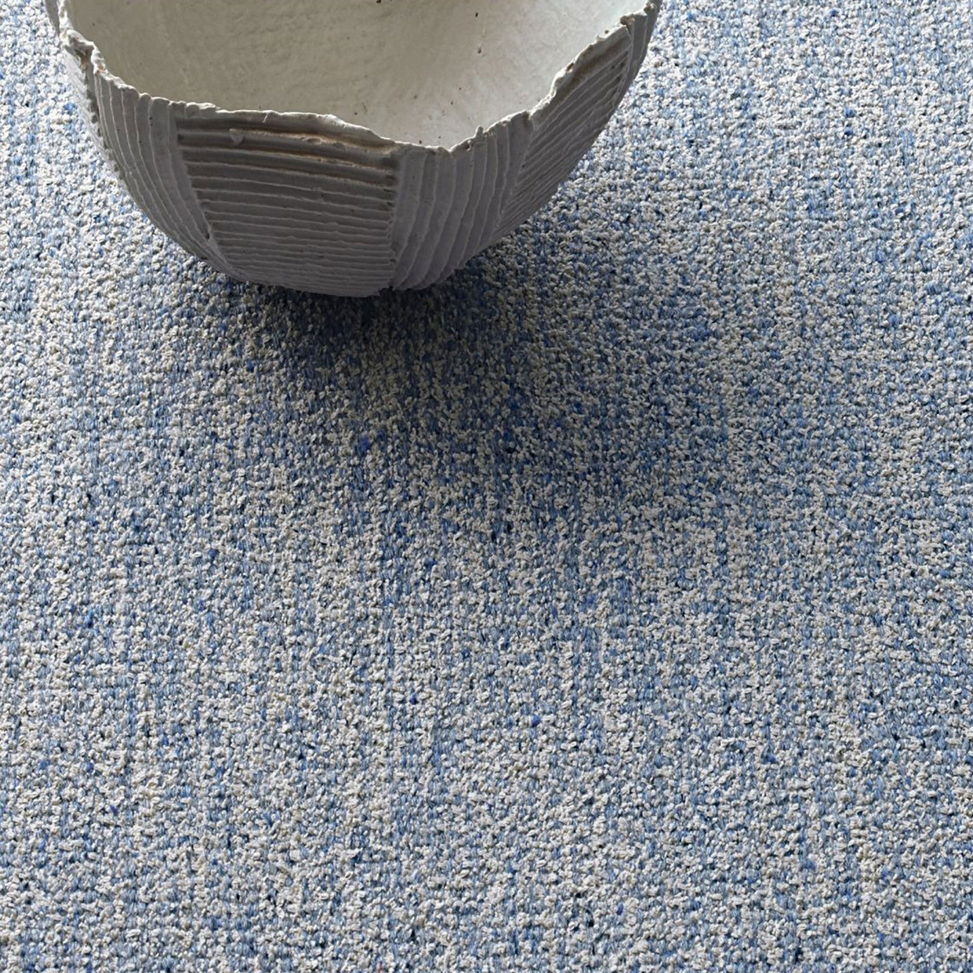 Iris rug style in off white and light blue colored mottled twisted flat weave with a clay bowl atop