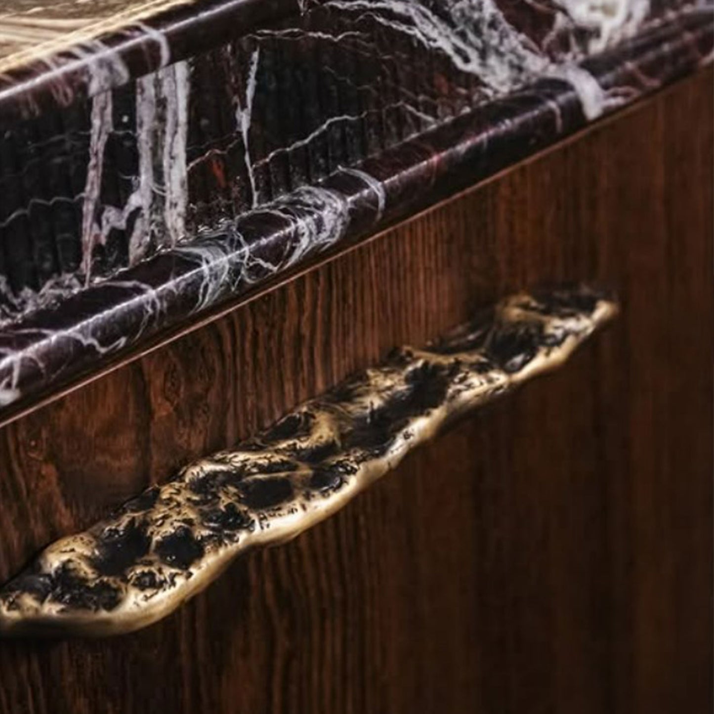 Close-up of a wooden cabinet with a organic-patterned handle and brass finish.