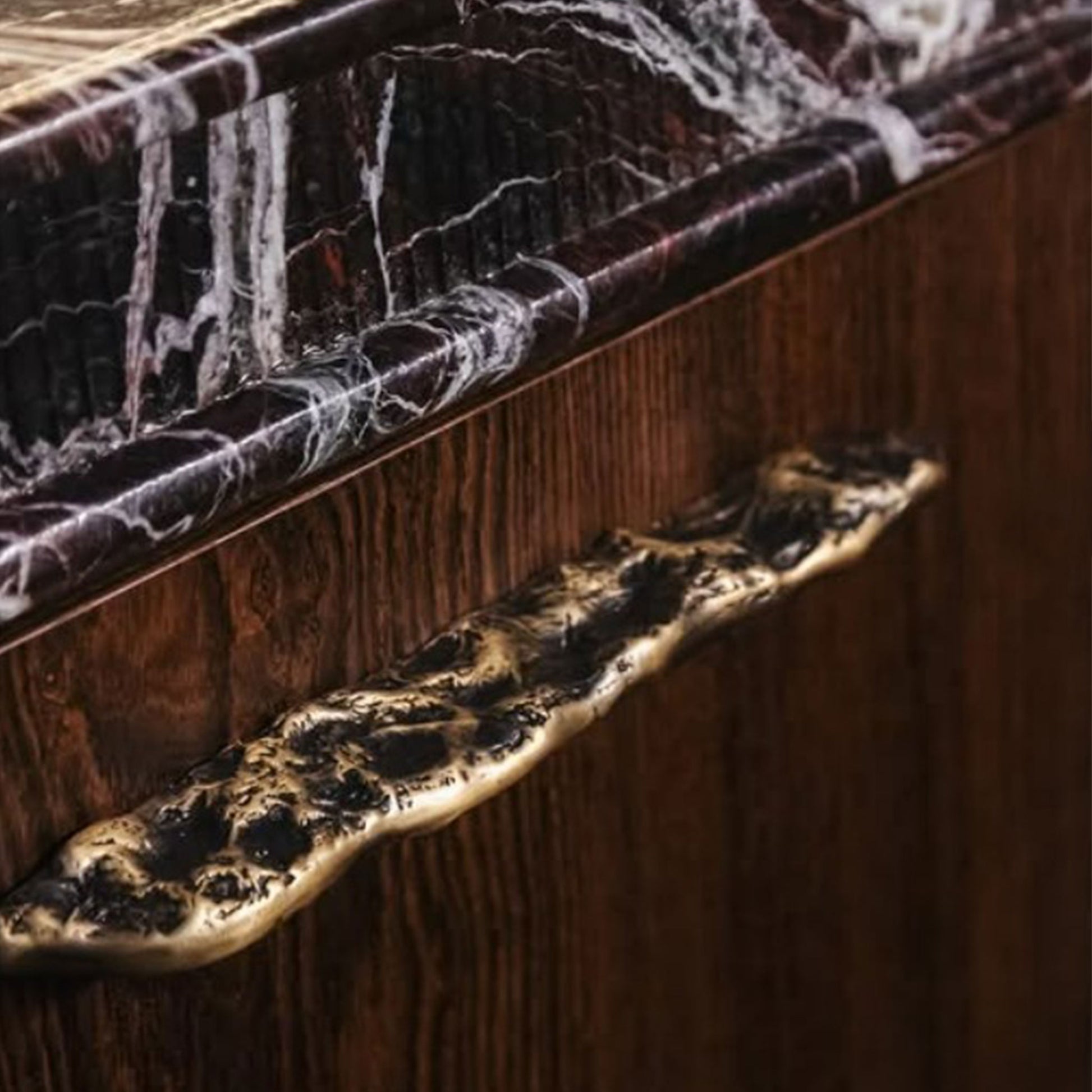 Close-up of a wooden cabinet with a organic-patterned handle and brass finish.