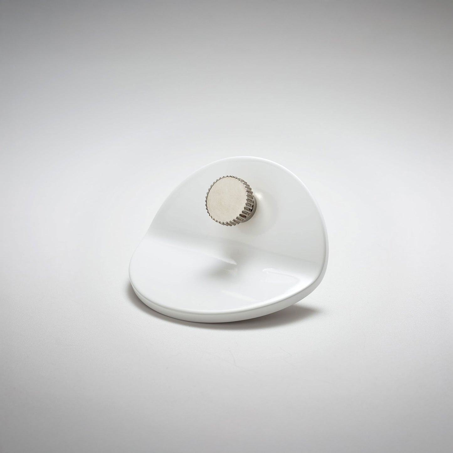 A polished white metal cabinet pull with a smooth curved and bent body with a small ridged circular knob, on a light gray background.