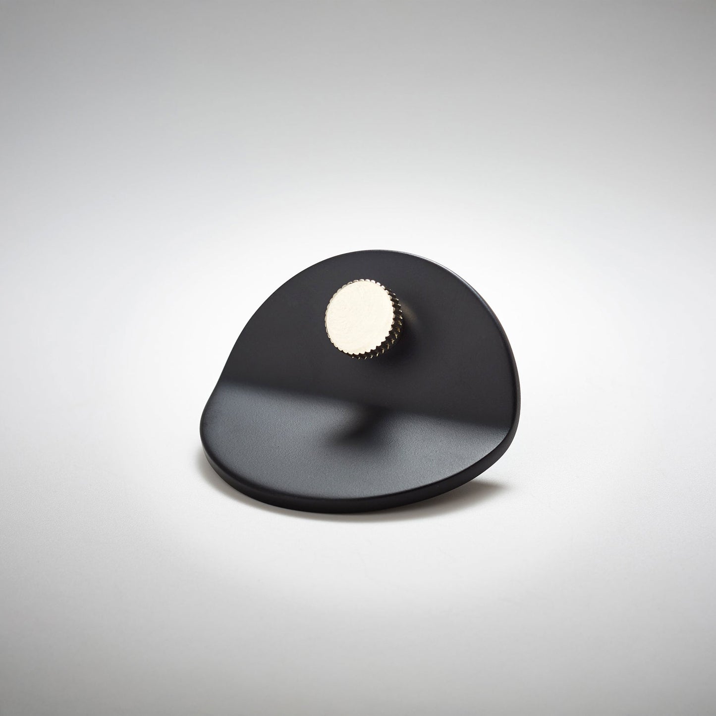 A polished matte black metal cabinet pull with a smooth curved and bent body with a small ridged circular knob, on a light gray background.