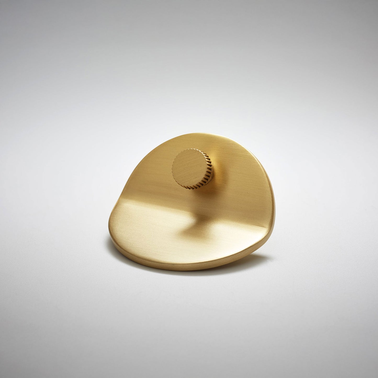 A polished gold-toned satin brass metal cabinet pull with a smooth curved and bent body and a small ridged circular knob, on a clean light gray background.