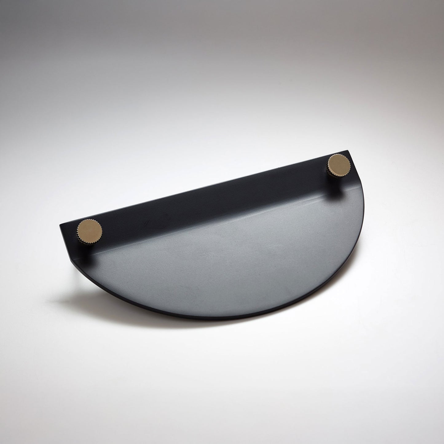 A modern semi-circular cabinet pull in a black finish, featuring two small round gold-toned details on the top edges, on a neutral background.