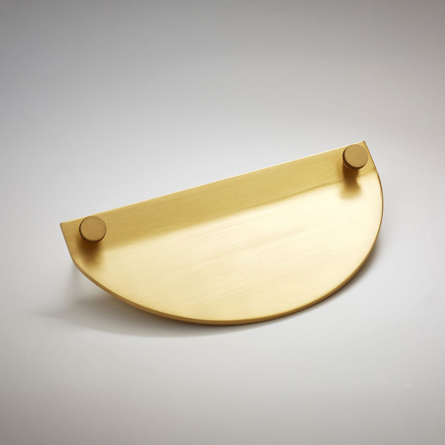 A modern semi-circular cabinet pull in a satin brass finish, featuring two small round gold-toned details on the top edges, on a neutral background.