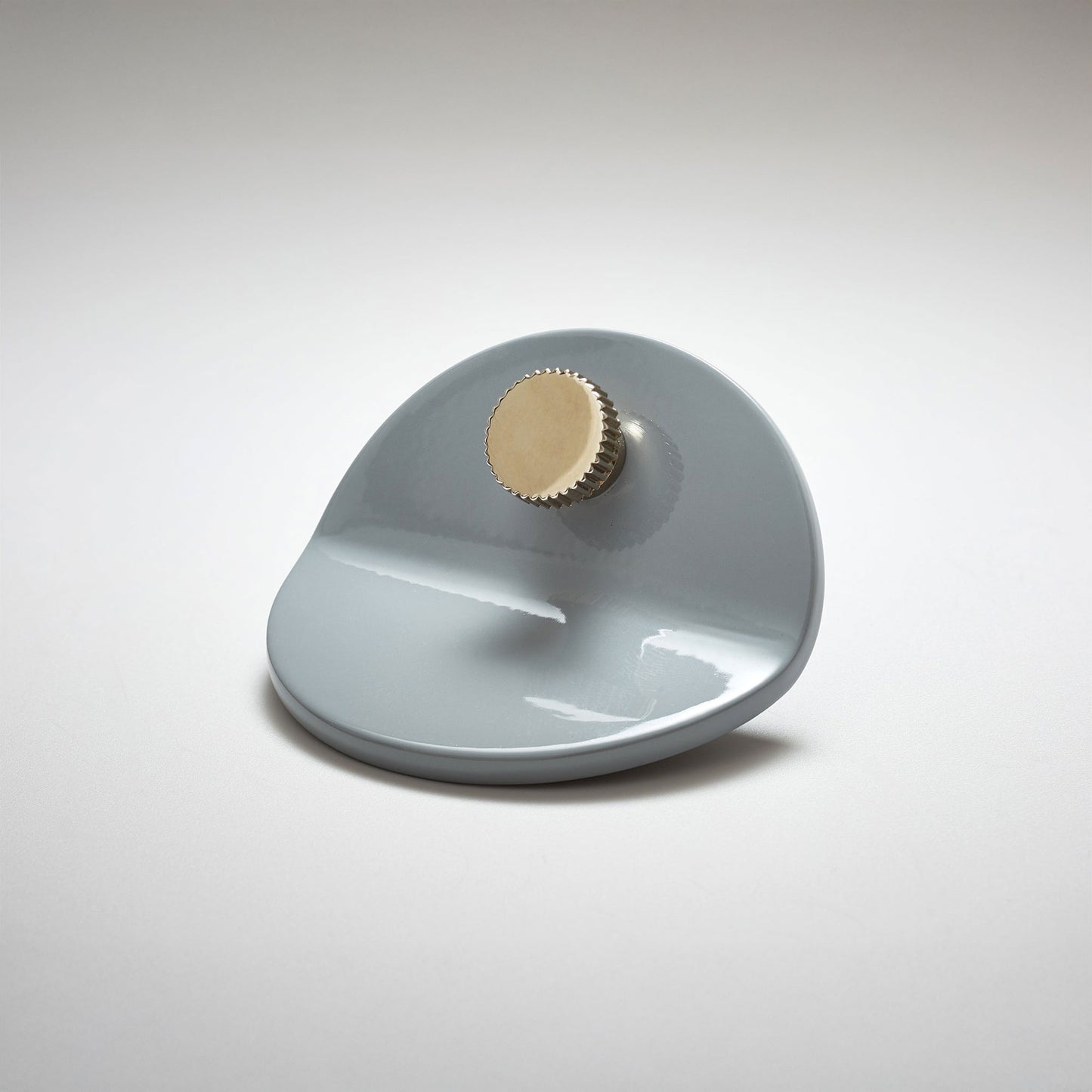 A shiny gray powder coated, bent circle metal cabinet pull handle with a small, round, brass detail on top photographed on a white background.