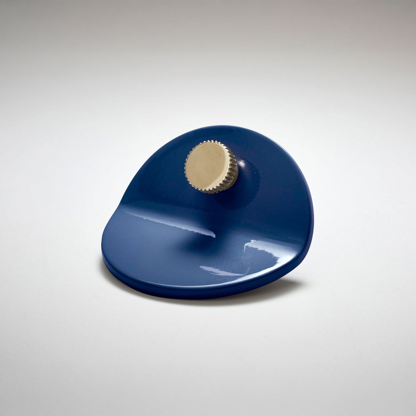 A shiny navy blue powder coated, bent circle metal cabinet pull handle with a small, round, brass detail on top photographed on a white background.