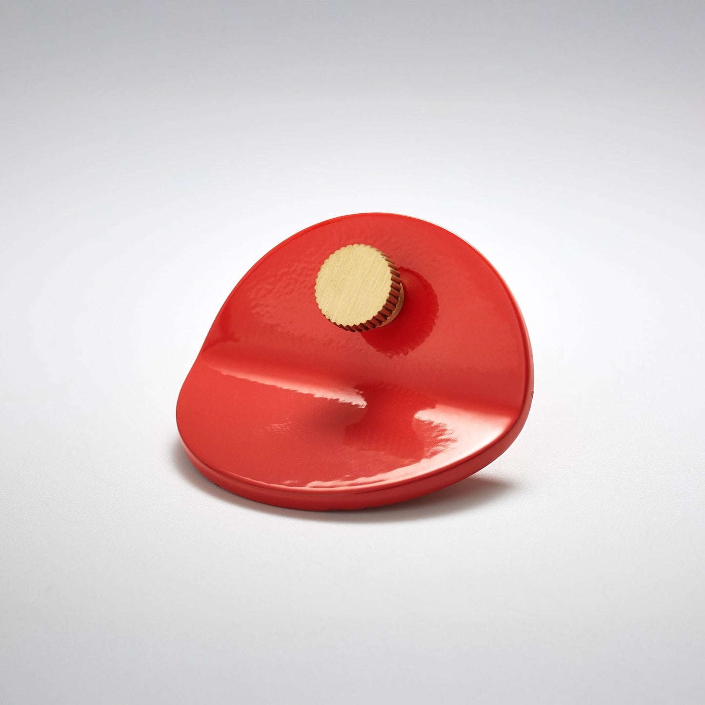 A glossy red, bent circle cabinet pull handle with a small, round, knob detail on top photographed on a white background.