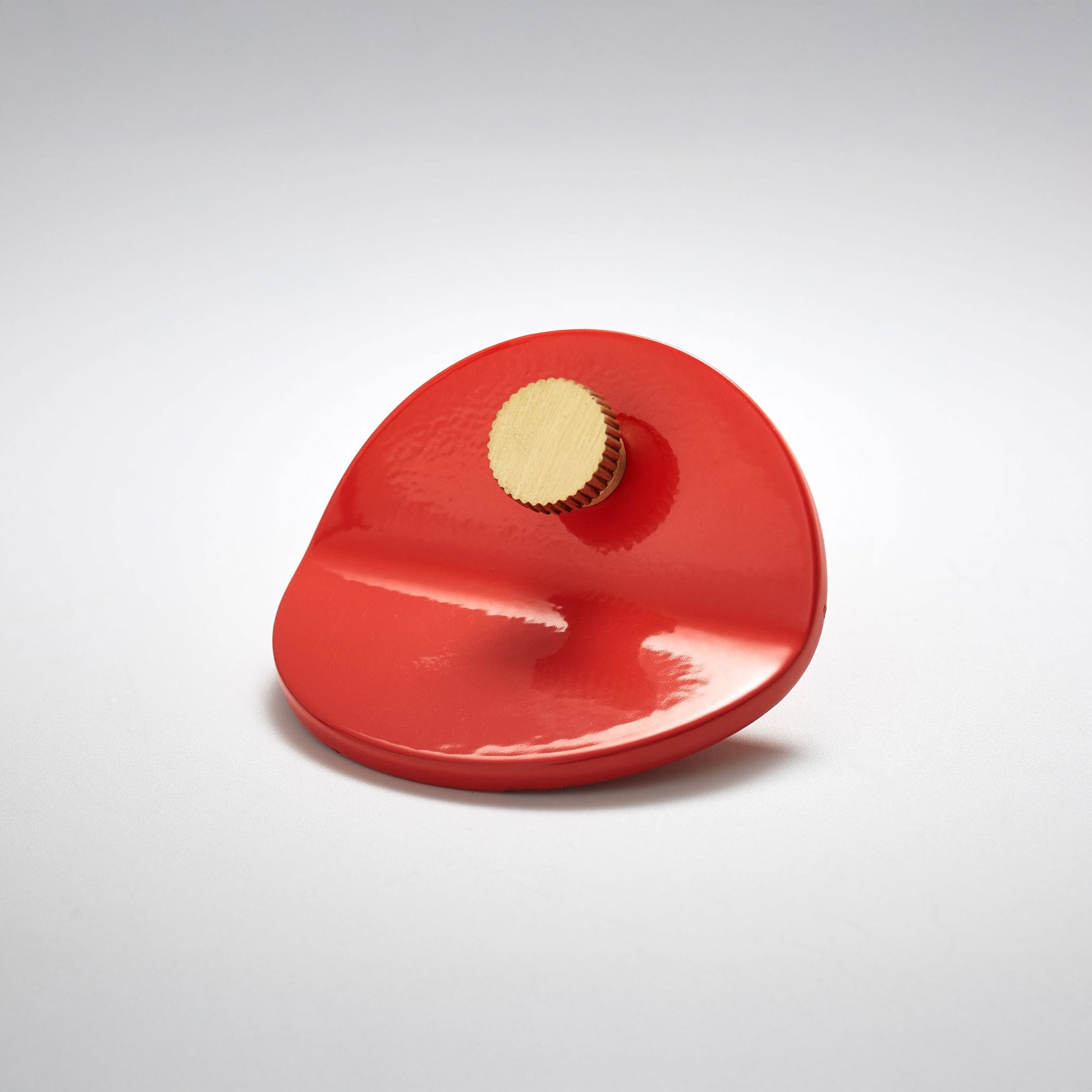 A glossy red, bent circle cabinet pull handle with a small, round, knob detail on top photographed on a white background.
