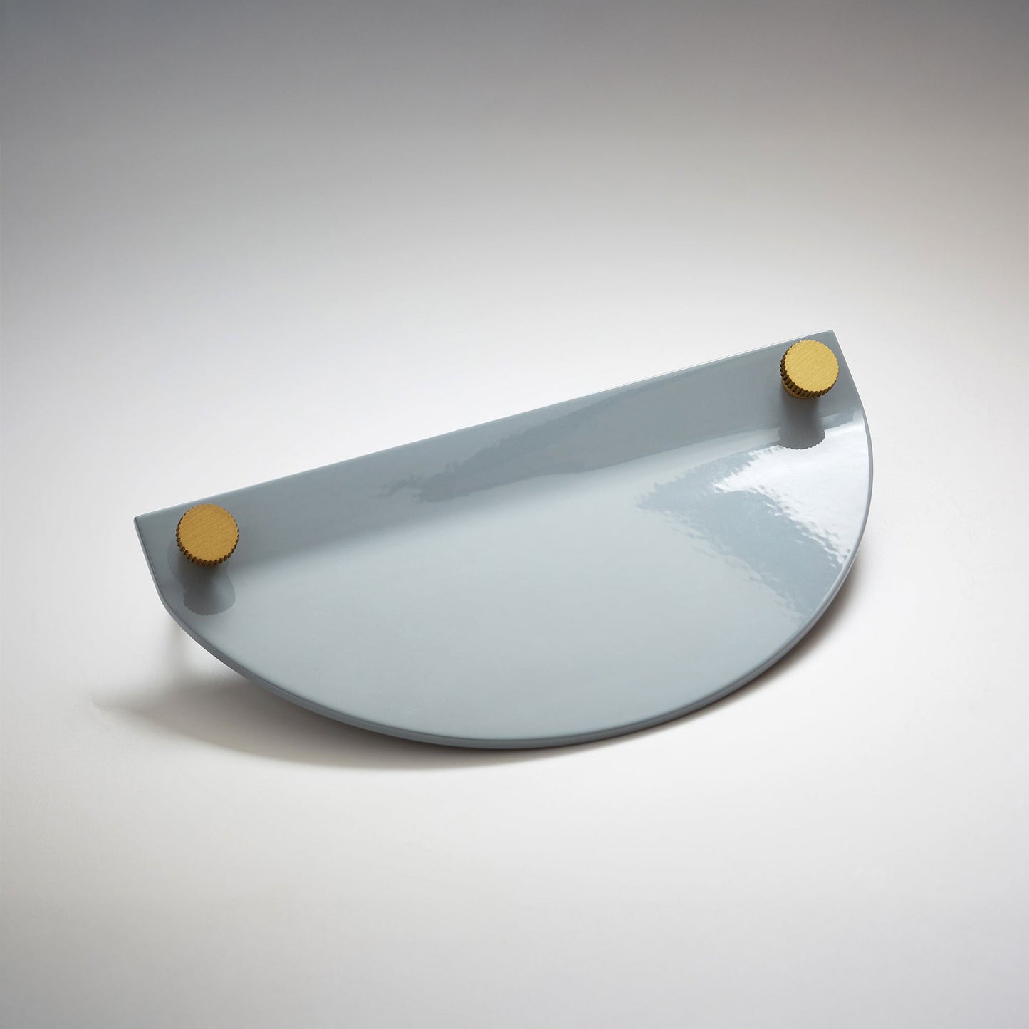 A shiny gray powder coated, semi circle metal cabinet pull handle with a small, round, brass details on top corners photographed on a white background.