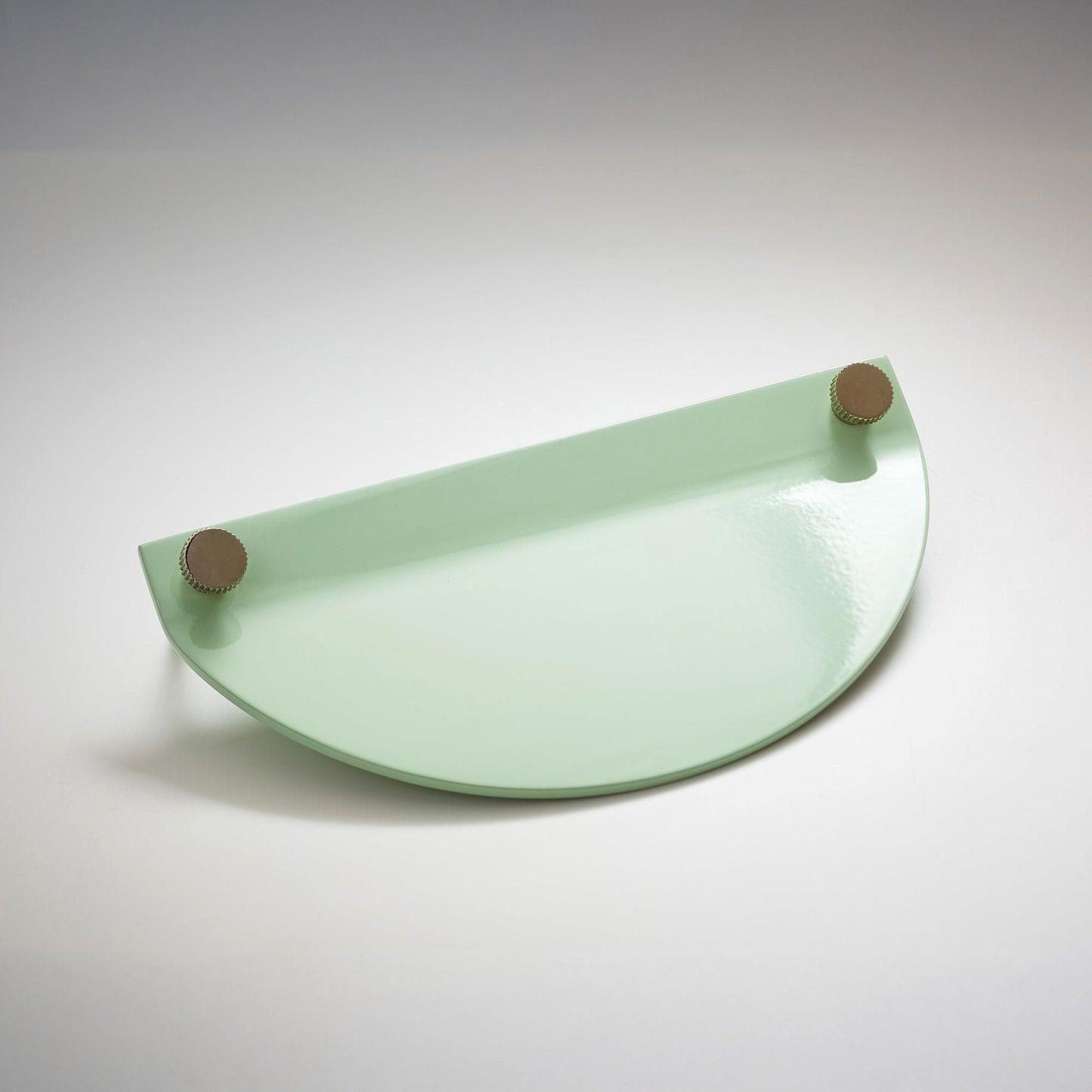 A shiny mint green powder coated, semi circle metal cabinet pull handle with a small, round, brass details on top corners photographed on a white background.