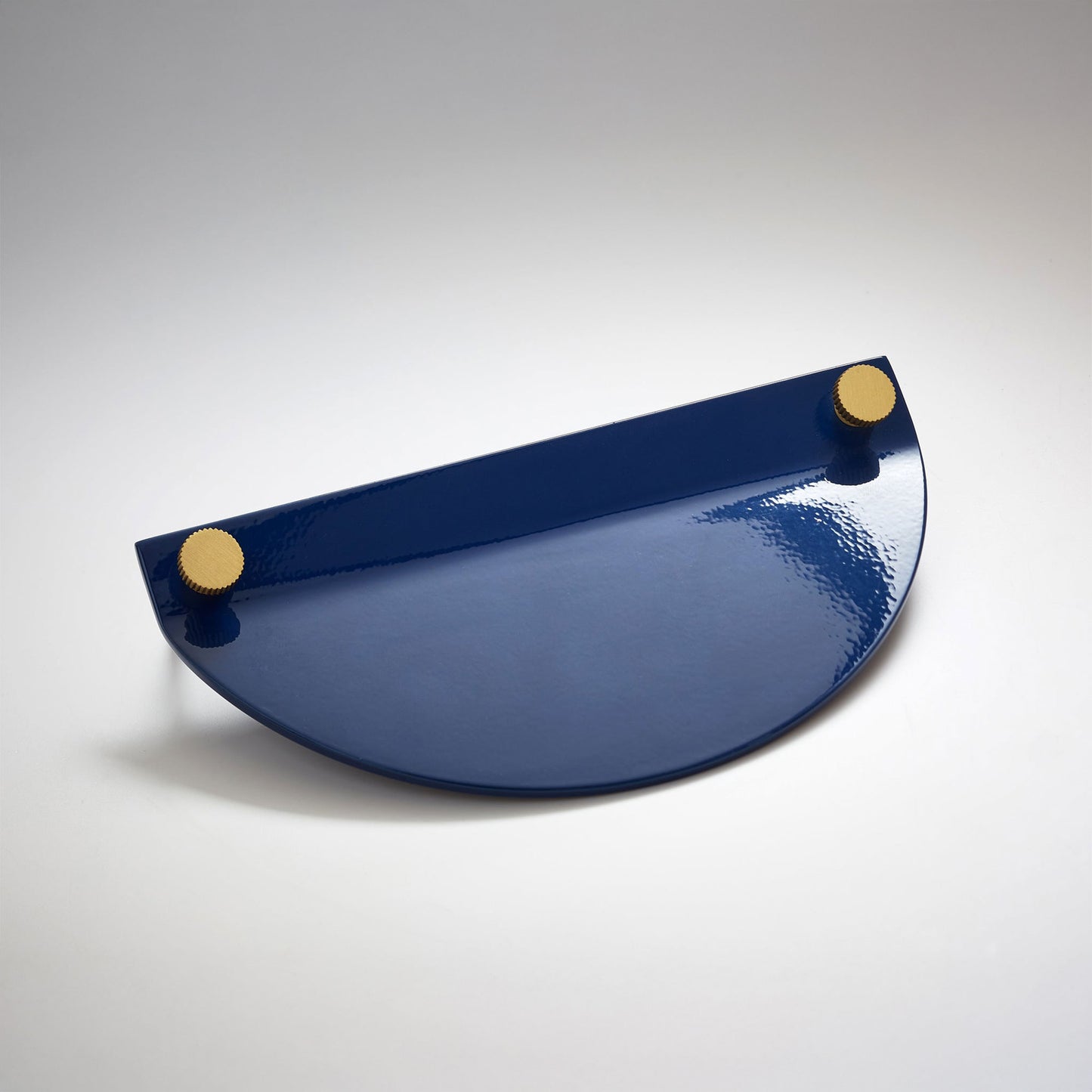 A shiny navy blue powder coated, semi circle metal cabinet pull handle with a small, round, brass details on top corners photographed on a white background.