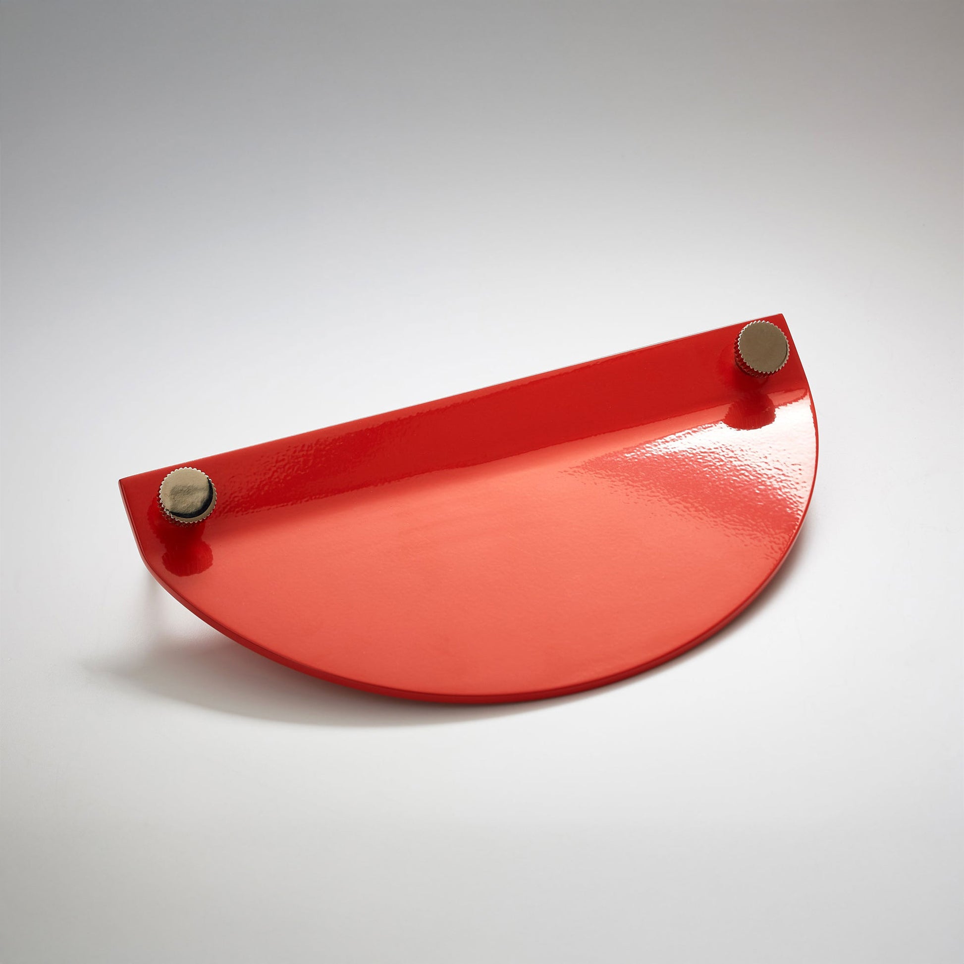 A shiny red powder coated, semi circle metal cabinet pull handle with a small, round, brass details on top corners photographed on a white background.