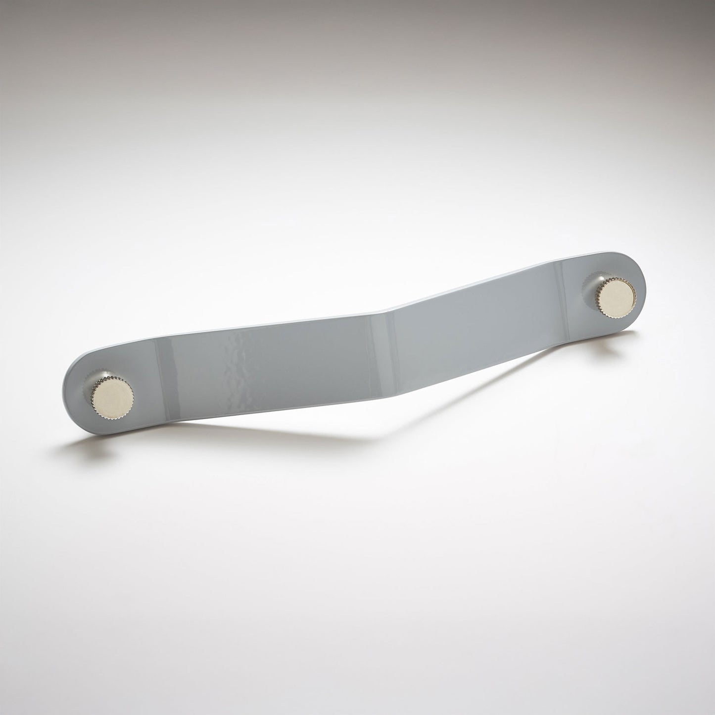 A shiny gray powder coated, long bent rectangular metal cabinet pull handle with two small, round, brass details on each corner photographed on a white background.