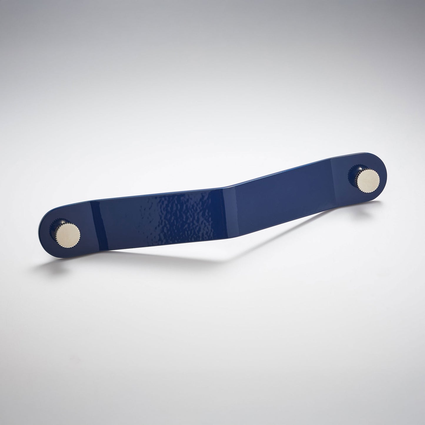 A shiny navy blue powder coated, long bent rectangular metal cabinet pull handle with two small, round, brass details on each corner photographed on a white background.