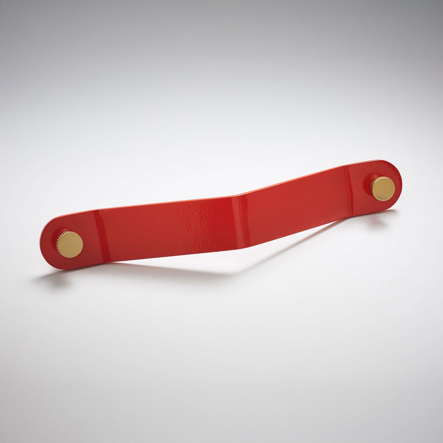 A shiny red powder coated, long bent rectangular metal cabinet pull handle with two small, round, brass details on each corner photographed on a white background.