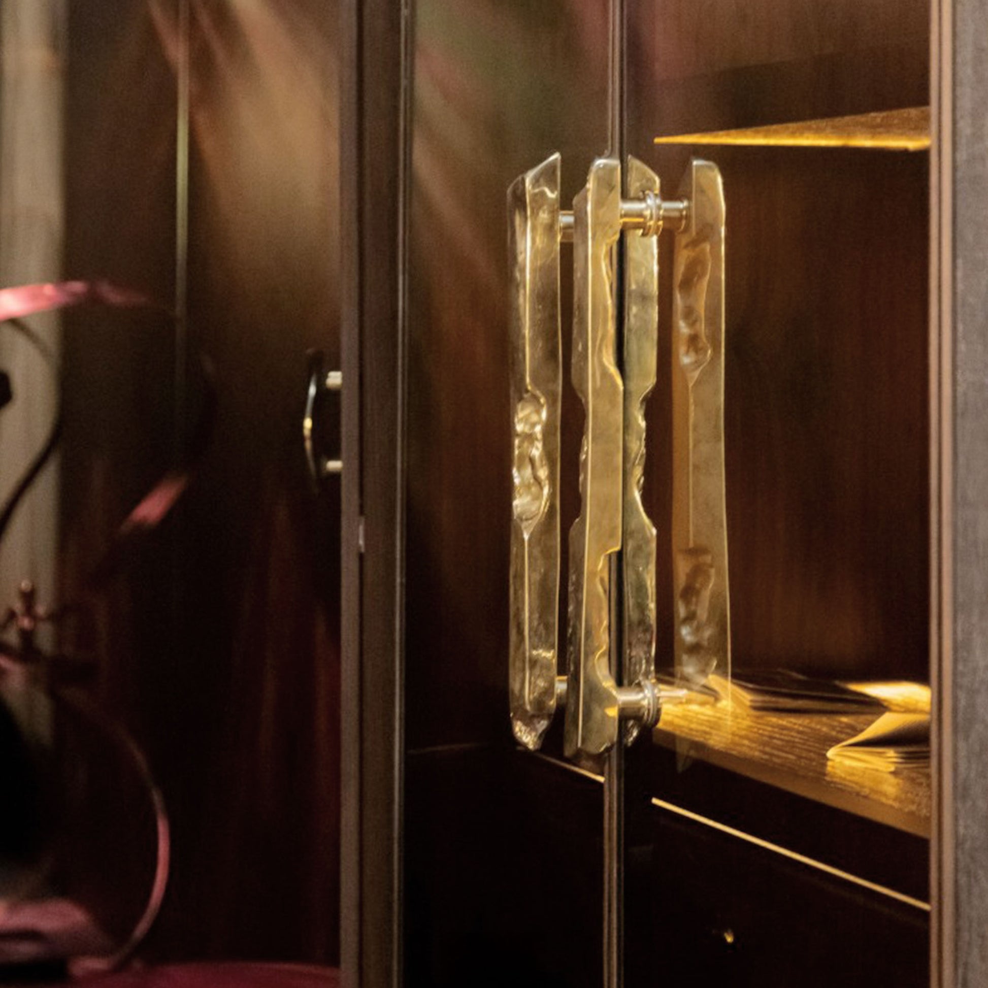 Close-up of a wooden cabinet with glass doors and unlacquered brass organic linear handles.