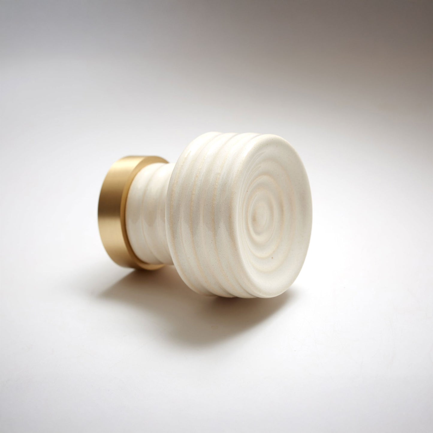 Off-white ceramic cabinet knob with gold accent on a white background.