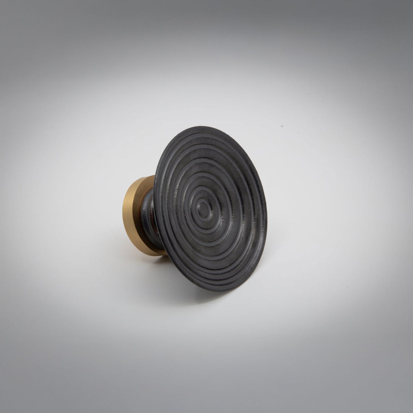 A round ceramic cabinet knob or pull with a black concentric ring patterned top and a gold-toned cylindrical base, photographed on a light gray background.