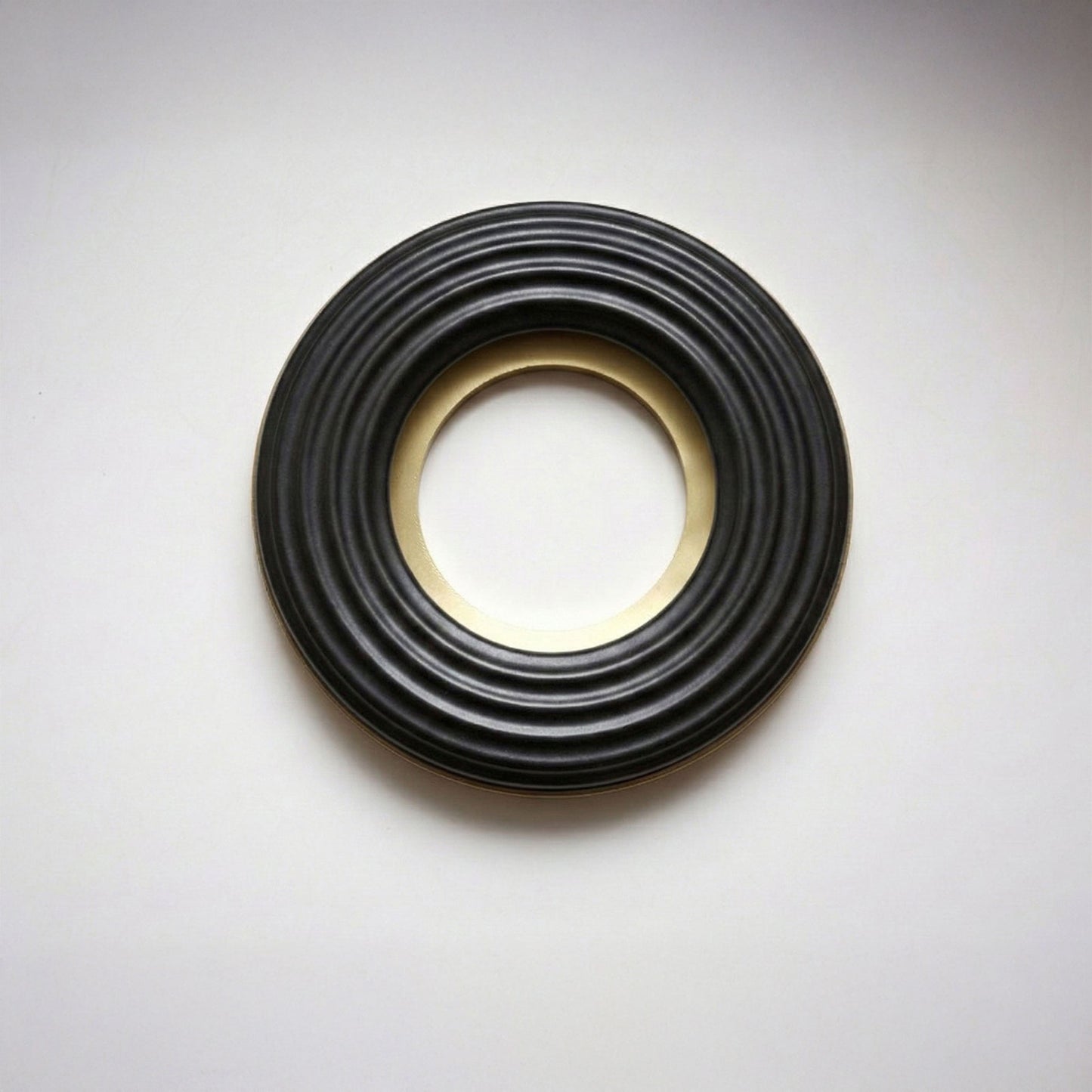 A large donut-shaped black ribbed ring with a polished gold-toned inner and outer rim, photographed on a light gray background.